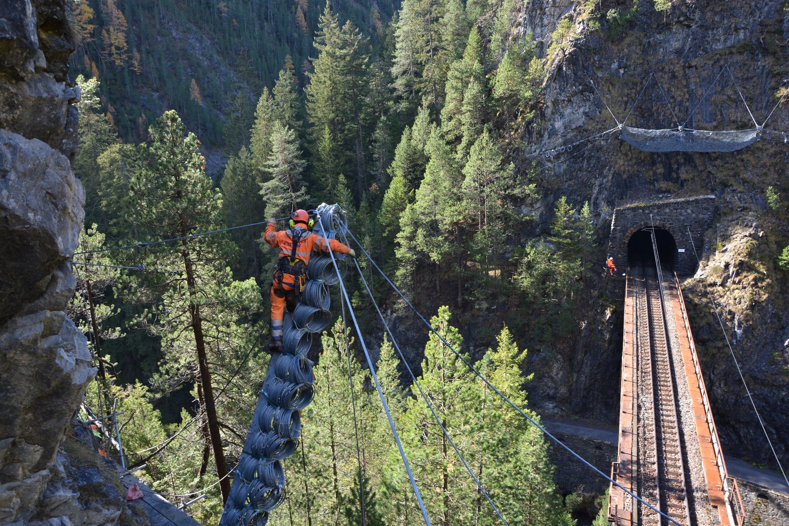 A worker on ropes installing mesh above a railway tunnel portal