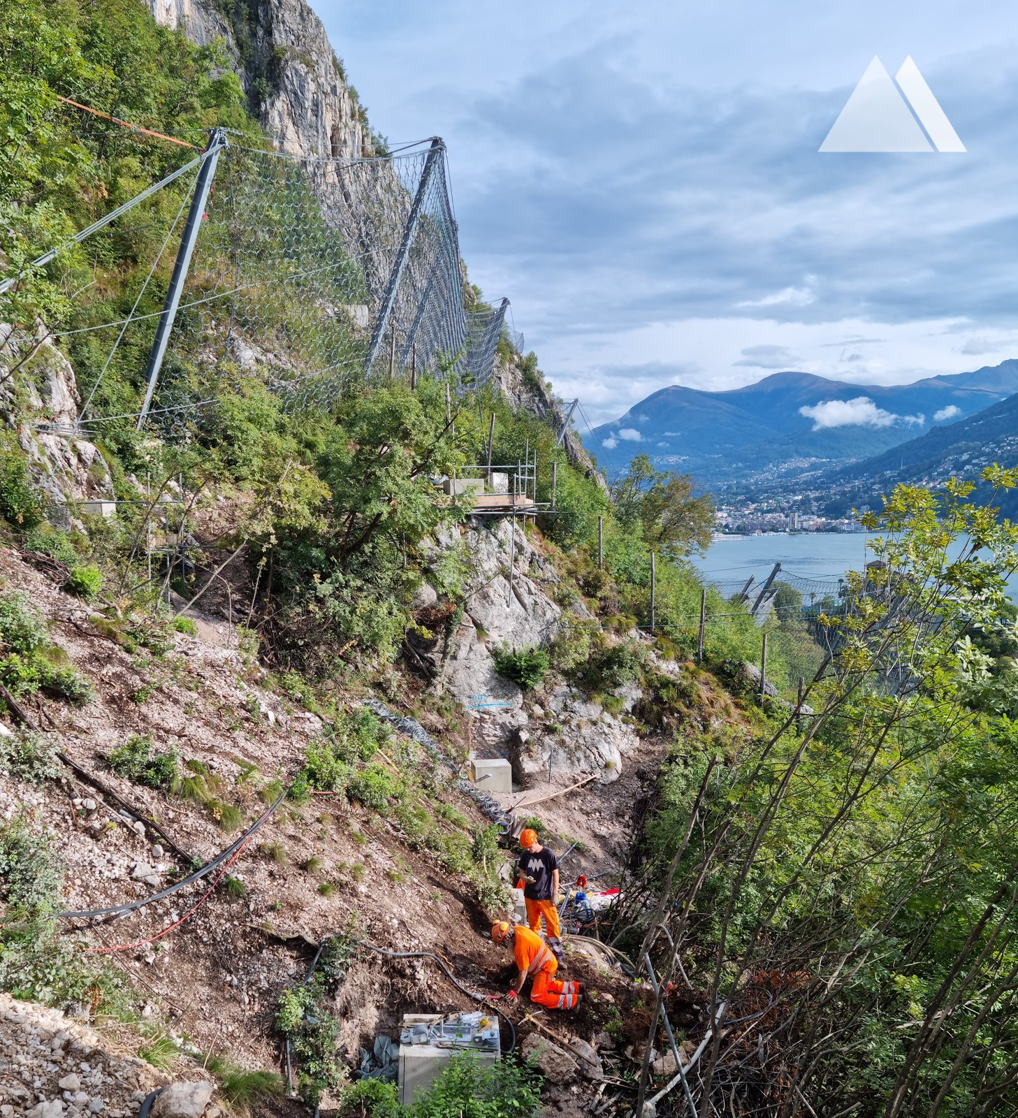 Steel mesh system on a steep wooded slope above a lake, a worker on ropes
