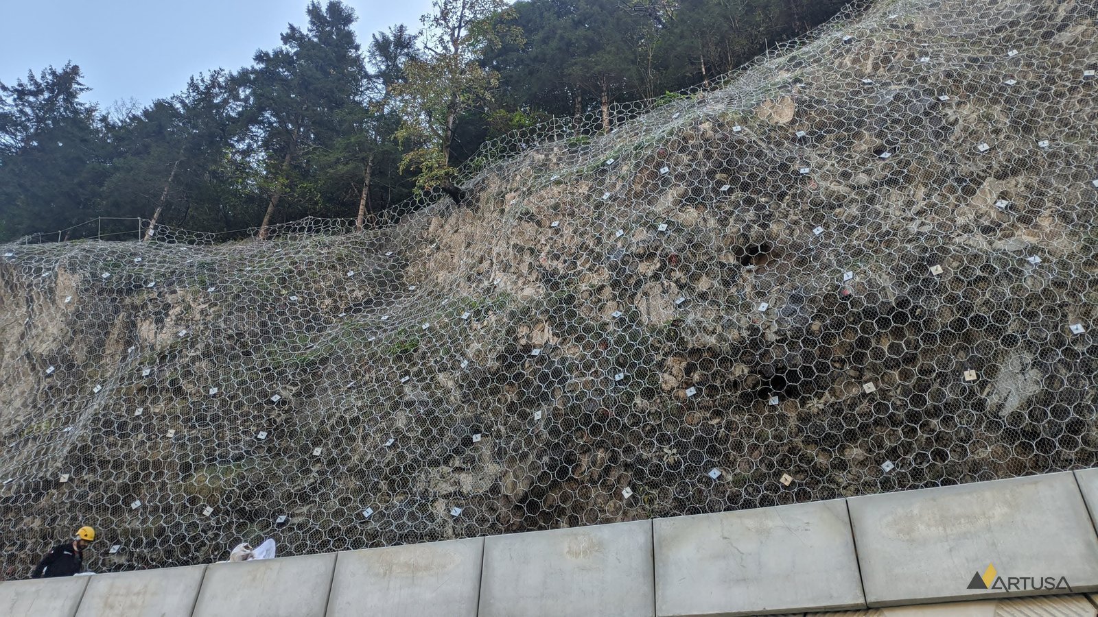 Mesh on a rock face above a retaining wall